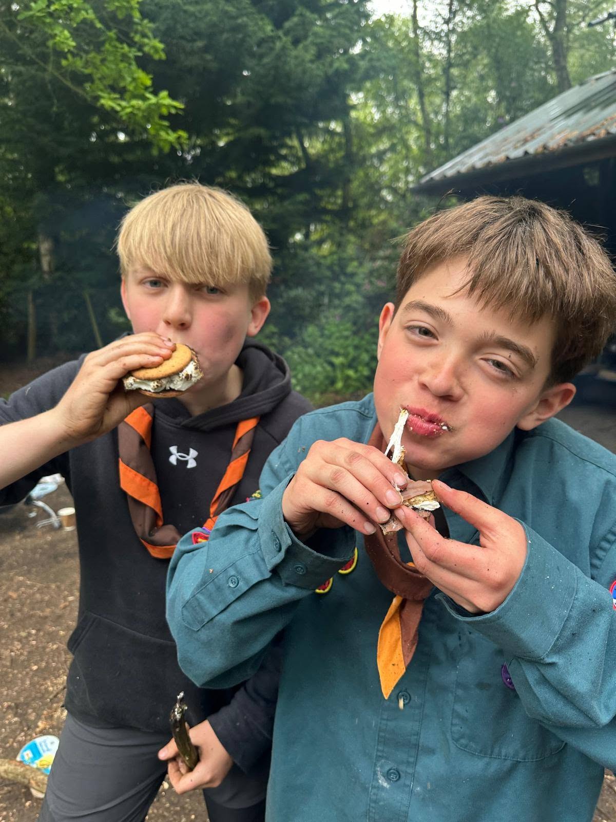 Two teen Scouts eating s'mores at YSAC (Snowball Plantation campsite(, both mid-bite with marshmallow stretching.
